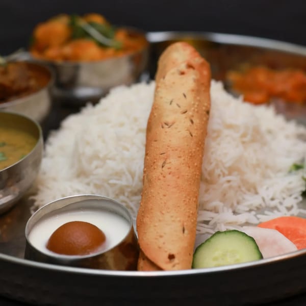 A Himalayan Doko thali with rice, papadum, gulab jamun, dal, and vegetable curries.