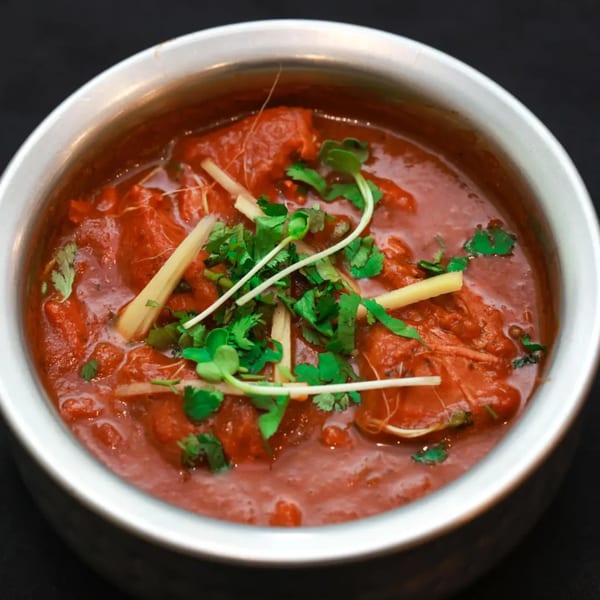Himalayan Doko's Indian chicken curry, garnished with fresh cilantro and ginger, in a metal bowl.