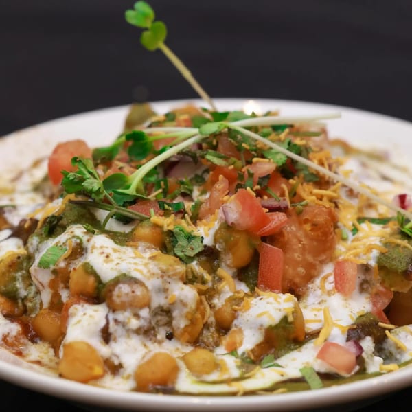 A vibrant Indian chaat dish, topped with chickpeas, tomatoes, yogurt, green chutney, and microgreens.