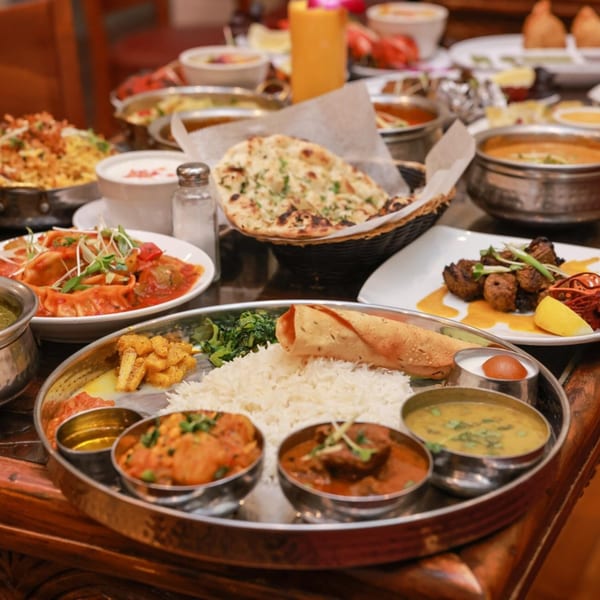 A table laden with various Indian dishes, including a thali, naan, momos, and curries.