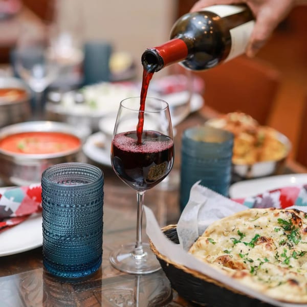 Red wine being poured into a glass at a table with Indian food and naan bread.