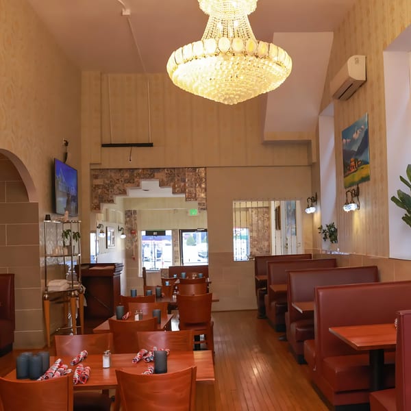 Interior of Himalayan Doko, an Indian restaurant, with wooden tables, red chairs, and booths under a large chandelier.
