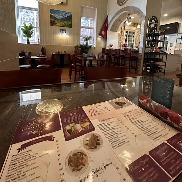 A Himalayan Doko menu on a glass table, with the restaurant's interior and bar in the background.