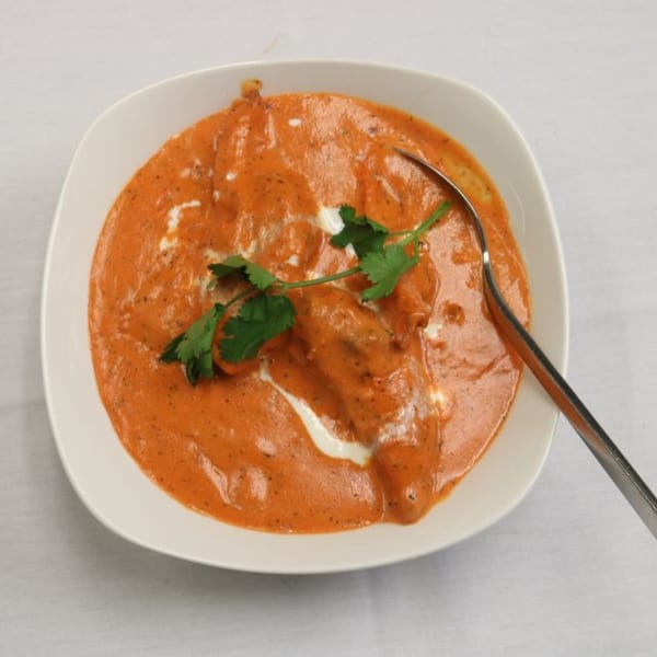 Himalayan Doko's Indian butter chicken, garnished with cilantro and a spoon, in a white bowl.