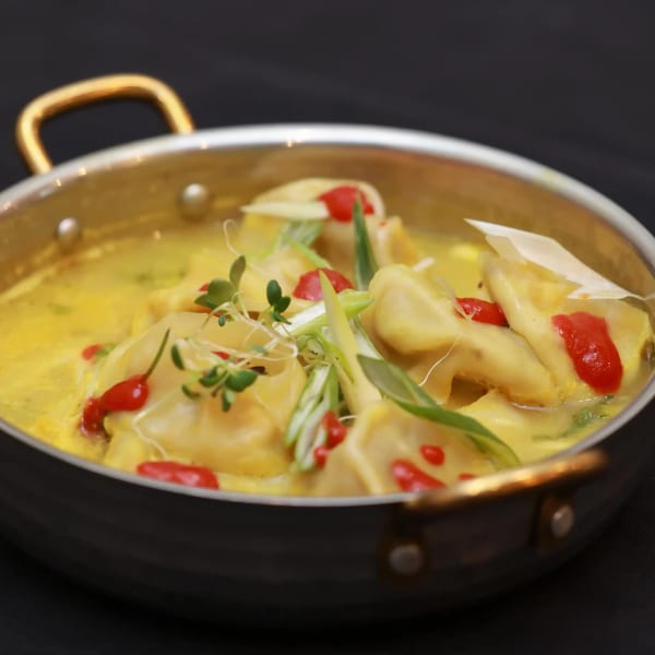 Himalayan Doko's momos in a creamy yellow sauce, garnished with red peppers and green onions.