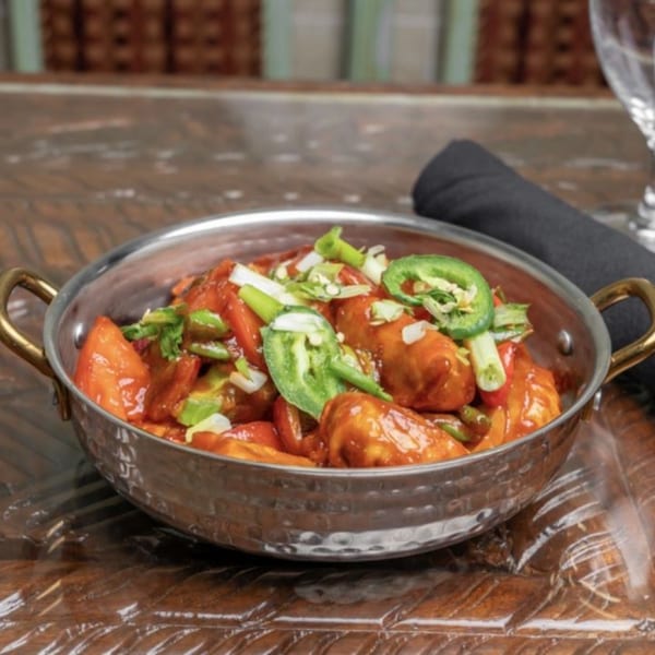 Himalayan Doko's Indian dish, chili chicken, served in a metal bowl with green peppers and onions.