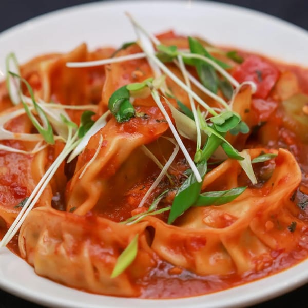 Himalayan Doko's momos, steamed dumplings in a rich red sauce, garnished with fresh herbs.