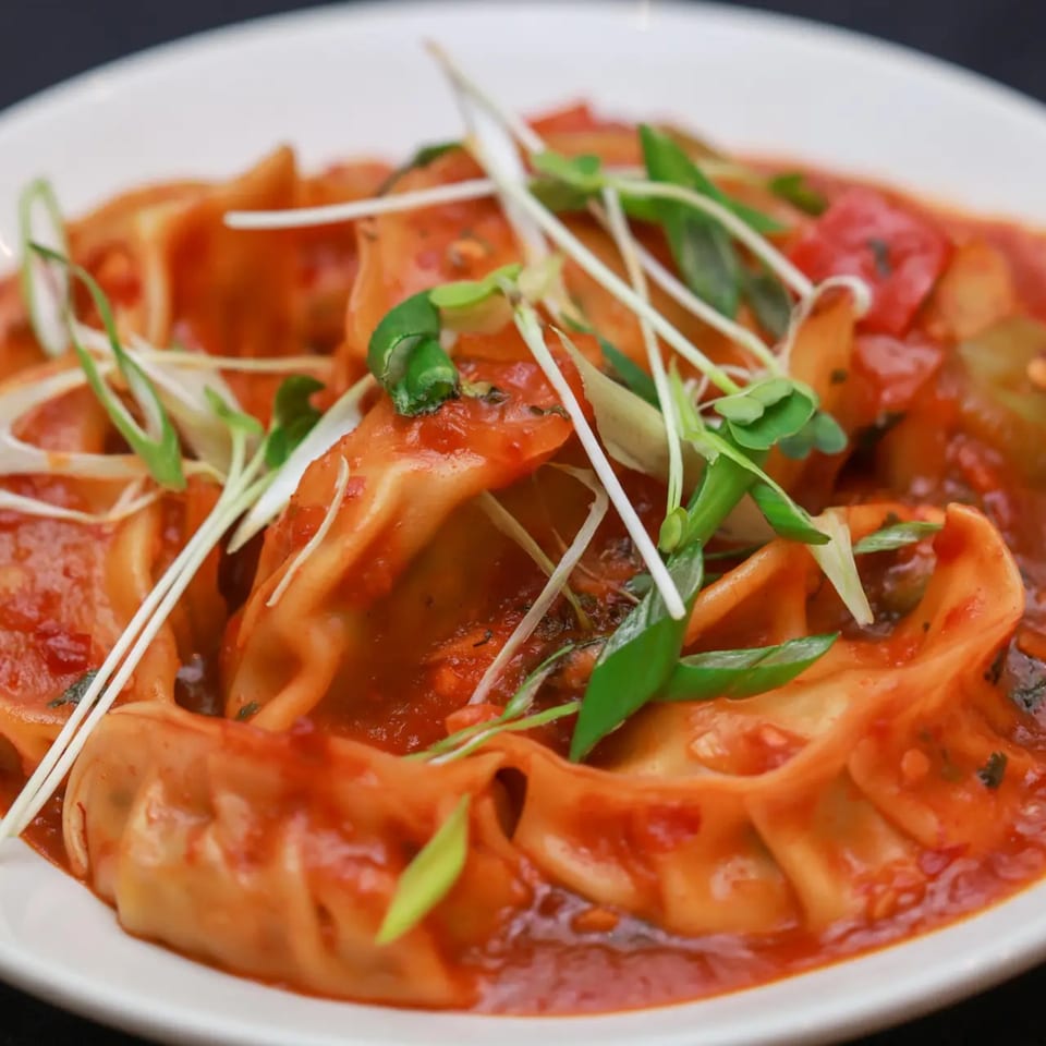 Himalayan Doko's momos, steamed dumplings in a rich red sauce, garnished with fresh herbs.