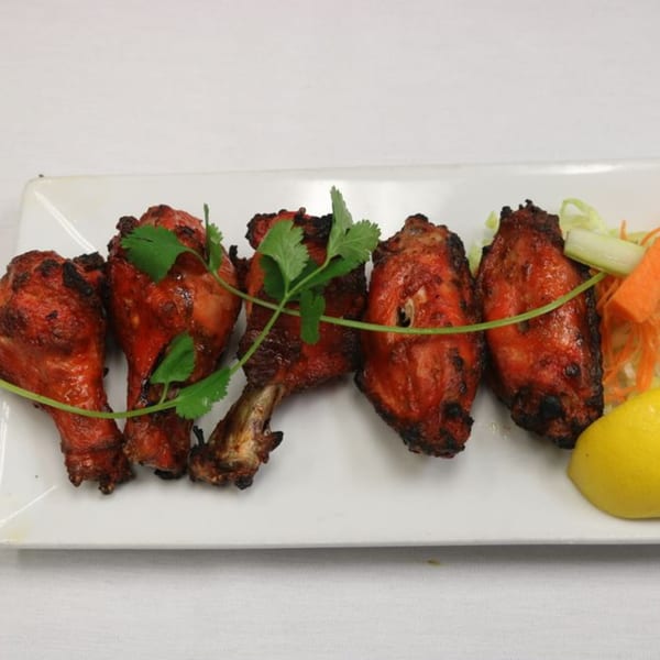 Five pieces of Indian tandoori chicken drumsticks garnished with cilantro, lemon, and salad.
