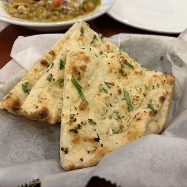 Three pieces of garlic naan bread, garnished with cilantro, served in a basket lined with white paper.
