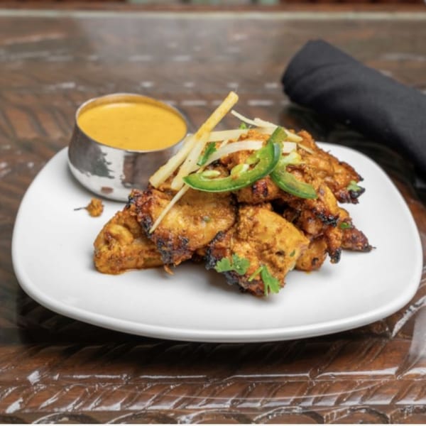 Himalayan Doko's Indian chicken tikka, garnished with jalapeños and ginger, served with a side of sauce.