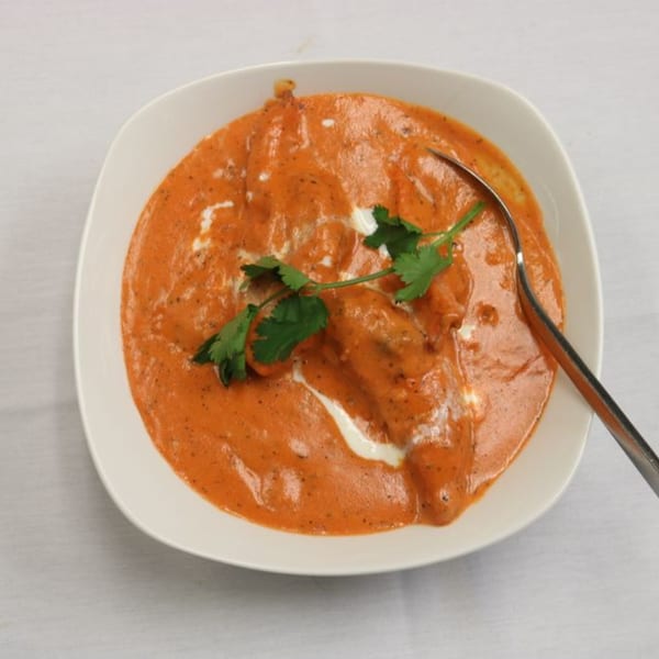 Himalayan Doko's Indian butter chicken, garnished with fresh cilantro and a spoon.