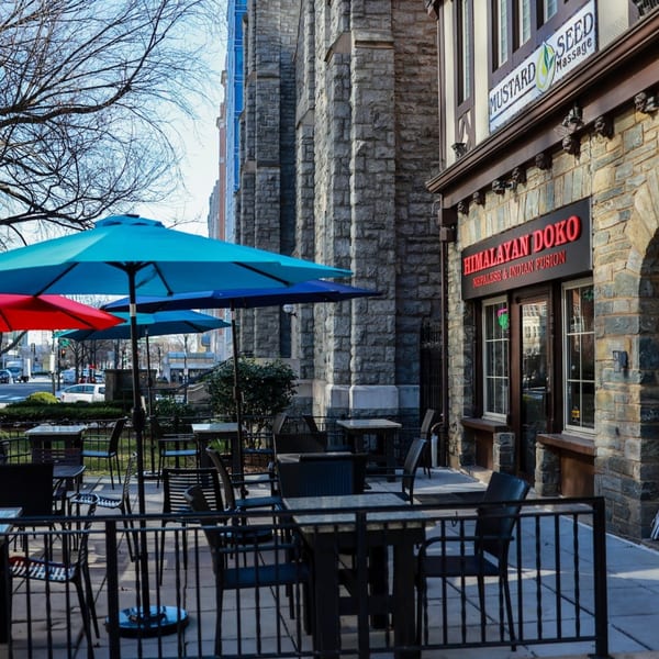 Himalayan Doko's outdoor patio with blue and red umbrellas, tables, and chairs on a sunny day.