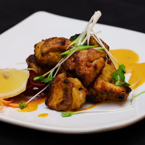 Indian chicken tikka with lemon, microgreens, and sauce on a white plate.