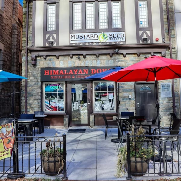 Himalayan Doko restaurant exterior with outdoor seating, red and blue umbrellas, and a stone facade.