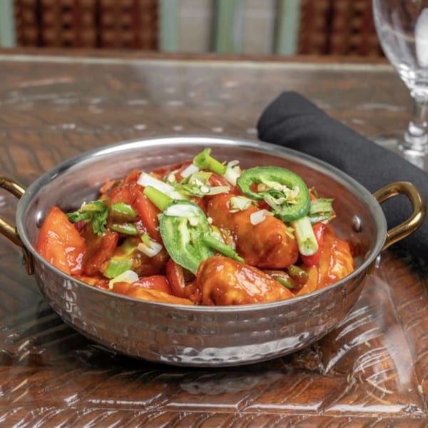 Himalayan Doko's Indian dish, chili chicken, in a metal bowl, garnished with green onions and jalapeños.