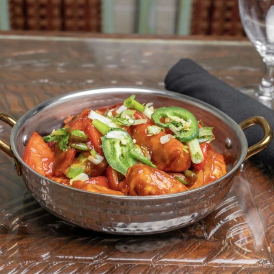 Himalayan Doko's Indian dish, chili chicken, in a metal bowl, garnished with green onions and jalapeños.