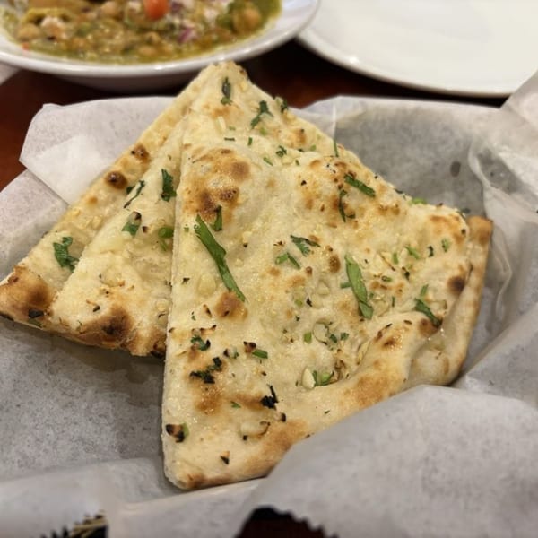 Three pieces of garlic naan bread, garnished with herbs, in a white paper-lined basket.