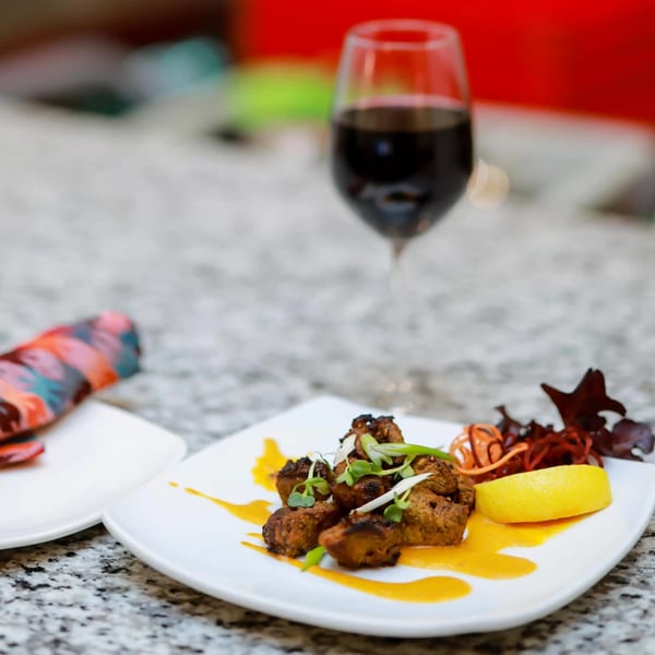 Indian lamb tikka with lemon, sauce, and greens, with a glass of red wine.