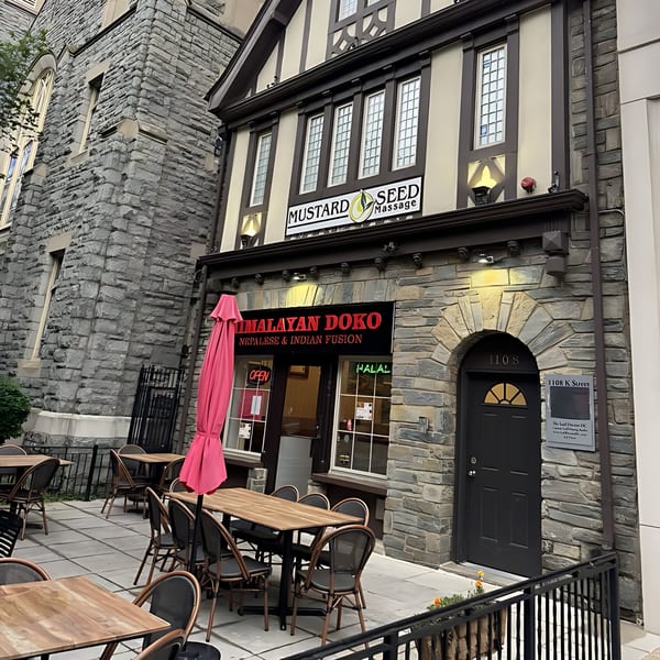 Himalayan Doko restaurant exterior with outdoor seating, a pink umbrella, and stone facade.