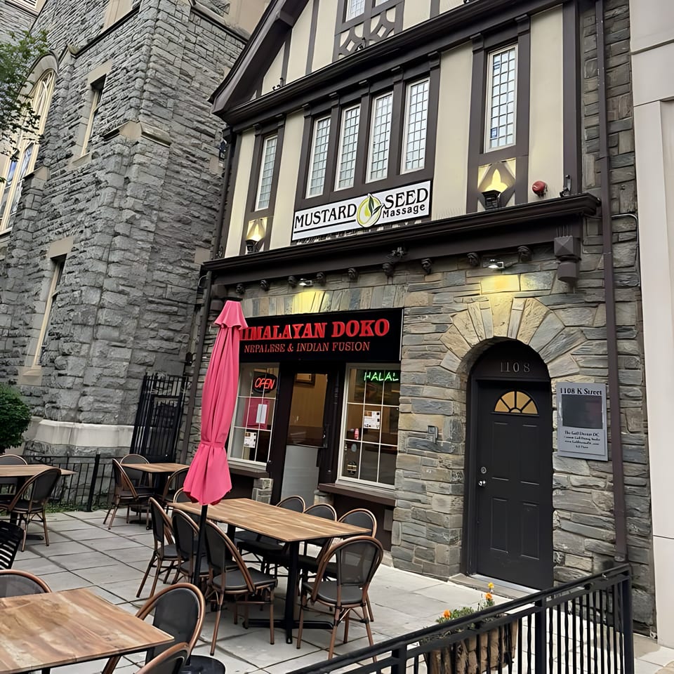 Himalayan Doko restaurant exterior with outdoor seating, a pink umbrella, and stone facade.