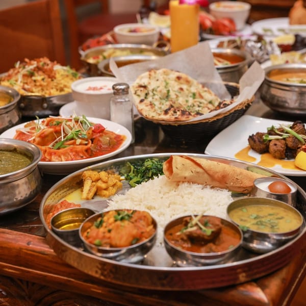 A table laden with various Indian dishes, including a thali, naan, momos, and curries.
