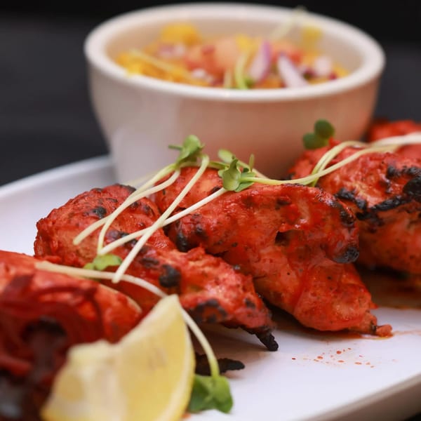 Himalayan Doko's Indian Tandoori Chicken, garnished with sprouts and a lemon wedge, with a side salad.